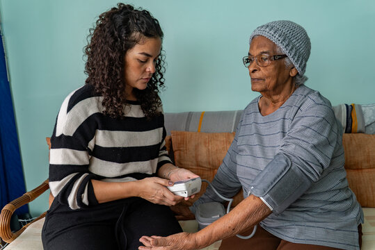 Candid Moment of Latina Woman Checking Blood Pressure of Afro Grandmother at Home