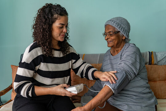Candid Moment of Latina Woman Checking Blood Pressure of Afro Grandmother at Home
