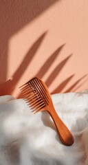 Light-brown wooden hair comb on a white cloth, sunlit, peach background