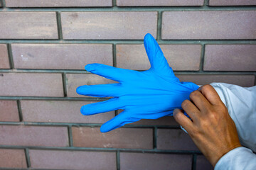 A person puts on blue latex gloves, preparing for a medical or sanitary task. The image focuses on...