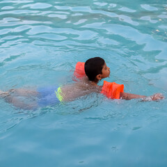 Happy Indian boy swimming in a pool, Kid wearing swimming costume along with air tube during hot...