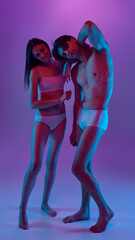Couple in white underwear under purple and blue lighting standing closely together. Concept of...