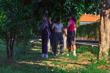 In a lush tropical park, four teenage girls smile while doing torso twist stretches together on the...