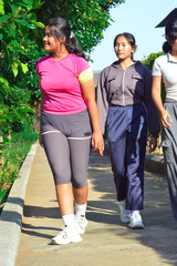 Obraz premium A pair of teen girls stroll along a quiet garden path, enjoying the calm atmosphere surrounded by lush tropical trees and green grass.