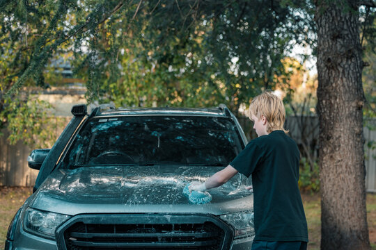 Teen boy hand washing car at home with blue sponge - Powered by Adobe