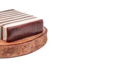 kue lapis A piece of traditional striped layer cake on a rustic wooden coaster, isolated on a white background with ample copy space