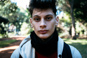 Young man wearing a black neck warmer and hoodie is posing in a park