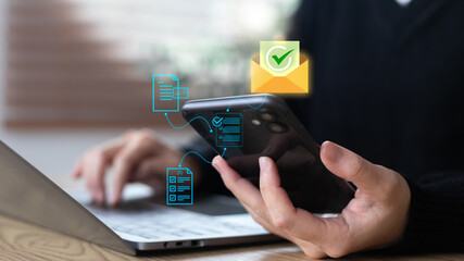 A hand using a smartphone and laptop with email and document approval icons, representing digital communication, document verification, online approval process, and business email management.