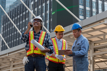 Group of Southeast Asian engineers wearing safety helmets and reflective vests reviewing...