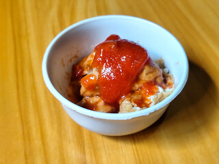 Pentol tofu served in a white bowl, pieces of tofu and meatballs covered in thick red chili sauce. Looks very delicious and delicious.
