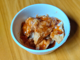 Pentol tofu served in a white bowl, pieces of tofu and meatballs covered in thick red chili sauce. Looks very delicious and delicious.