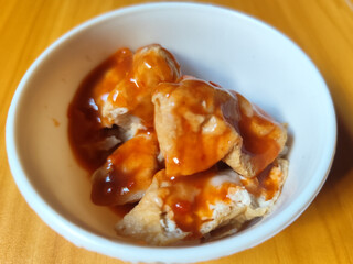 Pentol tofu served in a white bowl, pieces of tofu and meatballs covered in thick red chili sauce. Looks very delicious and delicious.