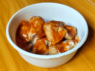 Pentol tofu served in a white bowl, pieces of tofu and meatballs covered in thick red chili sauce. Looks very delicious and delicious.