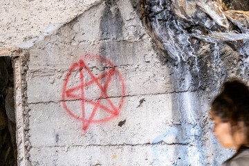 Graffiti-Pentagramm auf Bunkerwand mit unscharfer Passantin