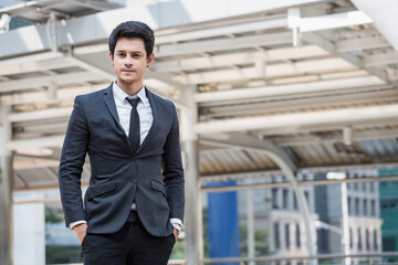 Southeast Asian businessman in dark suit and tie standing confidently in modern city business...