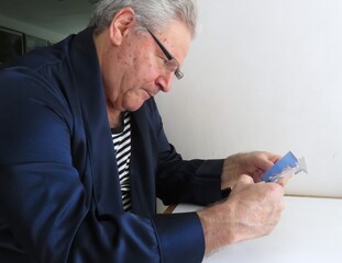 An elderly man with glasses sits at a table, deeply focused on a cutting an intricate design. It's...