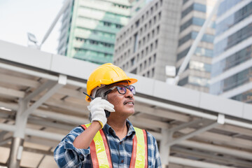 Southeast Asian construction engineer in safety helmet and reflective vest holding blueprint while...
