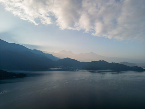 Aerial view of a serene lake reflecting mountains and clouds at sunrise. Misty atmosphere. - Powered by Adobe