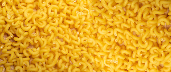 Raw yellow cavatappi pasta texture background top view. Pile of dry uncooked noodles pattern