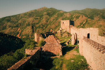 Ancient stone fortress ruins surrounded by green mountains under warm evening light