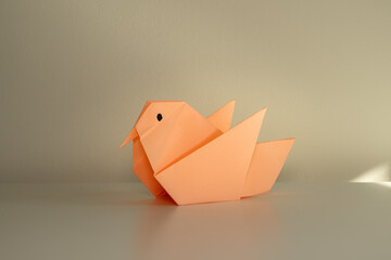 Paper bird figure folded from peach-colored paper on a light background
