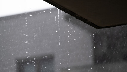 Rain falling from building roof edge during overcast weather