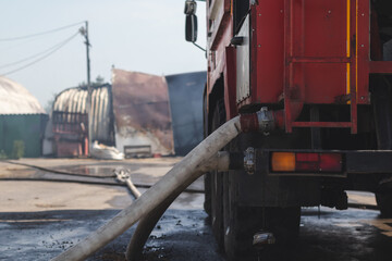 A fire engine with hoses attached against the backdrop of a burnt hangar