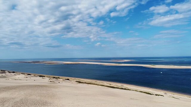 Aerial drone view of sandy dunes meeting the blue sea under a partly cloudy sky. Beach and coastline idea. Nature and landscape concept.
