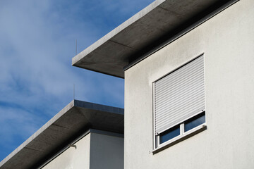 Detail of a white house facade with a flat roof and a window and roller shutter