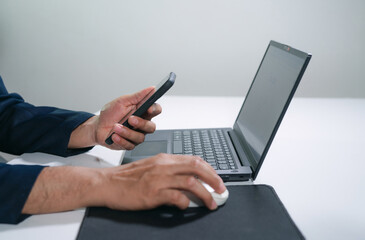 Fototapeta premium Business man using a laptop and a cell phone at the same time.