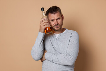 Man with bottle of whiskey suffering from hangover on beige background