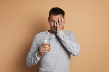 Man with glass of water suffering from hangover on beige background