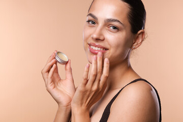 Young woman with lip balm on beige background