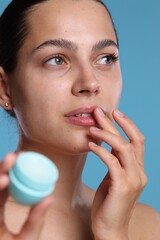 Young woman with lip balm on light blue background