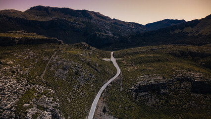 Winding mountain road at sunset captured from drone. Scenic asphalt road cuts through rocky hills...