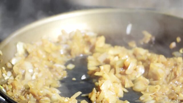 Close-up of wooden spatula mixing caramelised onions in a hot frying pan. Cooking and gourmet recipe idea. Kitchen preparation and food concept.