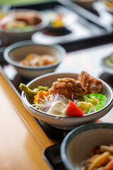 Close-up shot of Japanese small dishes (yorishoku) on a dark wooden table. Includes fried chicken, vegetables, and dipping sauces in small ceramic bowls. Warm lighting.