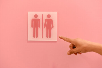 Close-up of a hand pointing at restroom symbols on a pink wall. Modern, playful setting with...