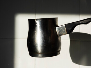 Cezve reflecting sunlight in a kitchen with white tiles