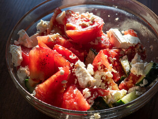 Fresh tomato and cucumber salad with feta cheese in a glass bowl