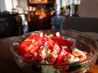 Tomato and feta salad in a glass bowl standing on a wooden table in a kitchen