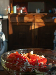 Preparing fresh greek salad with tomatoes, cucumber and feta cheese in a glass bowl