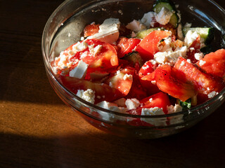 Fresh tomato and cucumber salad with feta cheese in glass bowl on wooden table