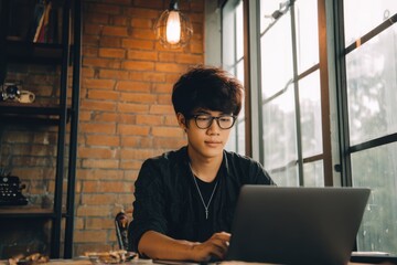 Young Asian Programmer Working on a Laptop in a Cozy Cafe During a Rainy Afternoon