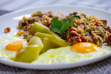 A traditional rustic Brazilian dish, known as Arrandinho, prepared with dried beef jerky, cassava flour, fresh cilantro, chayote salad and fried eggs.