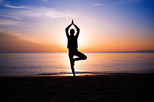 Person performing yoga tree pose on beach at sunset image