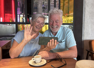 Video call concept. Smiling senior couple sharing a warm moment over coffee in a modern café using smartphone capturing the essence of love, connection, and active elderly retirement lifestyle