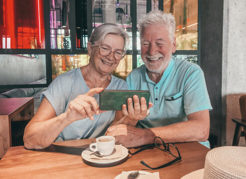 Smiling retired senior couple sharing a warm moment over coffee in a modern café using smartphone capturing the essence of love, connection, and active elderly retirement lifestyle
