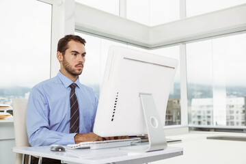 Fototapeta premium Businessman typing on all-in-one desktop computer in office corner with stack of papers, copy space