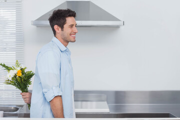 Smiling man turning toward hidden bouquet behind him in home kitchen with steel extractor hood